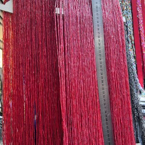 May include: Close-up of red beaded strands hanging vertically. A metal ruler is placed next to the strands, showing measurements up to 50 cm. The beads appear to be small and cylindrical, creating a textured, vibrant display.