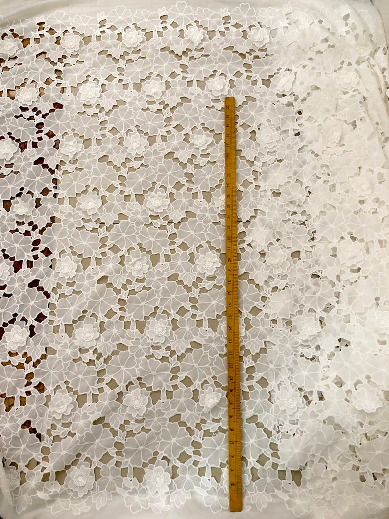May include: White cotton lace fabric with a floral pattern. The fabric is shown with a ruler measuring 30 inches.