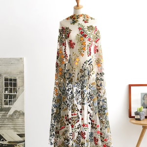 May include: A sheer white fabric with colourful embroidered flowers and leaves. The fabric is draped over a mannequin and has a floral pattern.