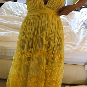May include: A yellow maxi dress with a V-neckline and floral embellishments. The dress has a fitted bodice and a flowing skirt.