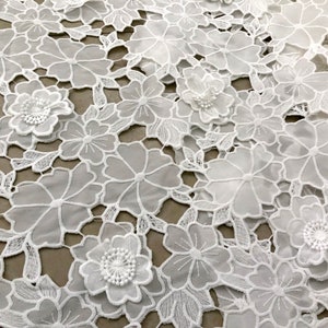 May include: White lace fabric with a floral design. The fabric has a delicate, intricate pattern with raised flowers.