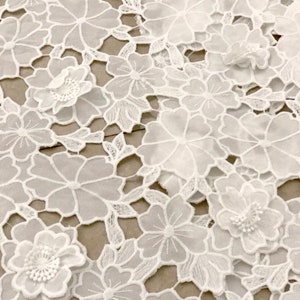 May include: White lace fabric with a floral pattern. The fabric is delicate and intricate, with small flowers and leaves.