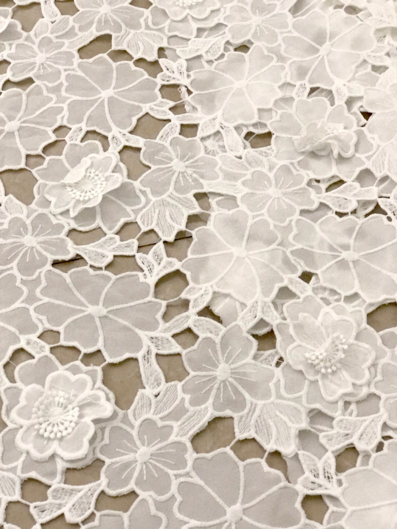 May include: White lace fabric with a floral pattern. The fabric is delicate and intricate, with small flowers and leaves.