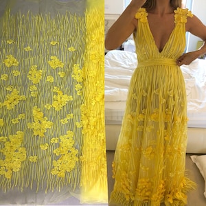 May include: Yellow floral lace fabric with a delicate pattern of small flowers. The fabric is sheer and has a soft, flowing texture.