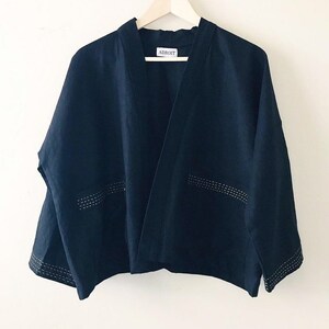 May include: A dark navy blue open-front jacket with long sleeves and a straight hem. The garment features white decorative stitching along the cuffs and the top of the two front pockets. A white label with the black text ADROIT is at the neck.