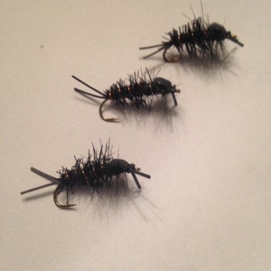 May include: Three black fly fishing lures with brown and gold accents. The lures are made of feathers and have a realistic insect design.