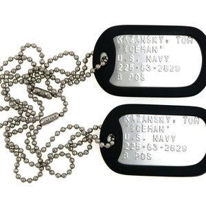 May include: Two silver dog tags with black rubber coating, attached to a silver ball chain. The tags are engraved with the text "KAZANSKY. TOM ICEHAN U.S. NAVY 225-63-2829 B POS".