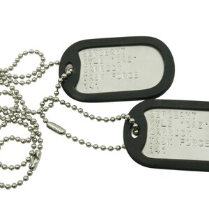 May include: Two military-style dog tags with ball chain necklaces. The tags are silver-colored with black rubber borders. Each tag has engraved text, including the name "Kyle 'SAZ' Carrick" and "Task Force 141".