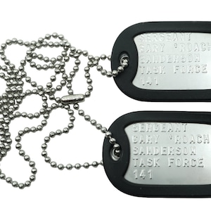 May include: Two silver military dog tags with black rubber coating on a silver ball chain. The tags read "SERGEANT GARY 'ROACH' SANDERSON TASK FORCE 141".