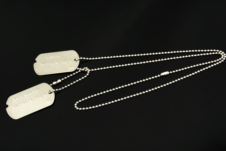 Puede incluir: Dos chapas de identificaci&oacute;n militares de plata en un collar de cadena de bolas de plata. La chapa superior dice "CHARLIE  1450172  1st  A  NO". La chapa inferior dice "WADE WILSON  1450172  1st  A  NO".