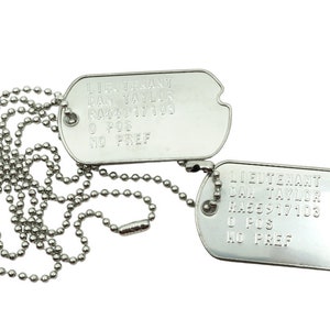 May include: Two silver military dog tags with a ball chain. The tags are engraved with the text "LIEUTENANT DAN TAYLOR" and "R000317103" and "O POS" and "NO PREF".