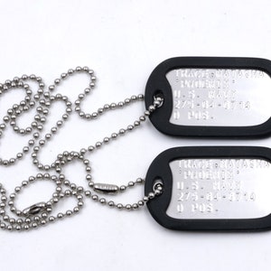 May include: Two black dog tags with silver lettering on a silver chain. The top tag reads "TRACE NATASHA PHOENIX U.S. NAVY 275-64-8714 O POS.". The bottom tag reads "TRACE NATASHA PHOENIX U.S. NAVY 275-64-6714 O POS."