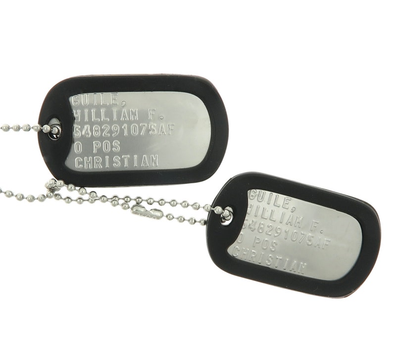 May include: Two black dog tags with silver lettering. The top tag reads "GUILE, WILLIAM F. 548291075AF 0 POS CHRISTIAN". The bottom tag reads "GUILE, WILLIAM F. 548291075AF 0 POS CHRISTIAN".