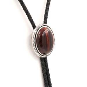 May include: A brown and black braided bolo tie with a silver oval pendant featuring a red tiger's eye stone.