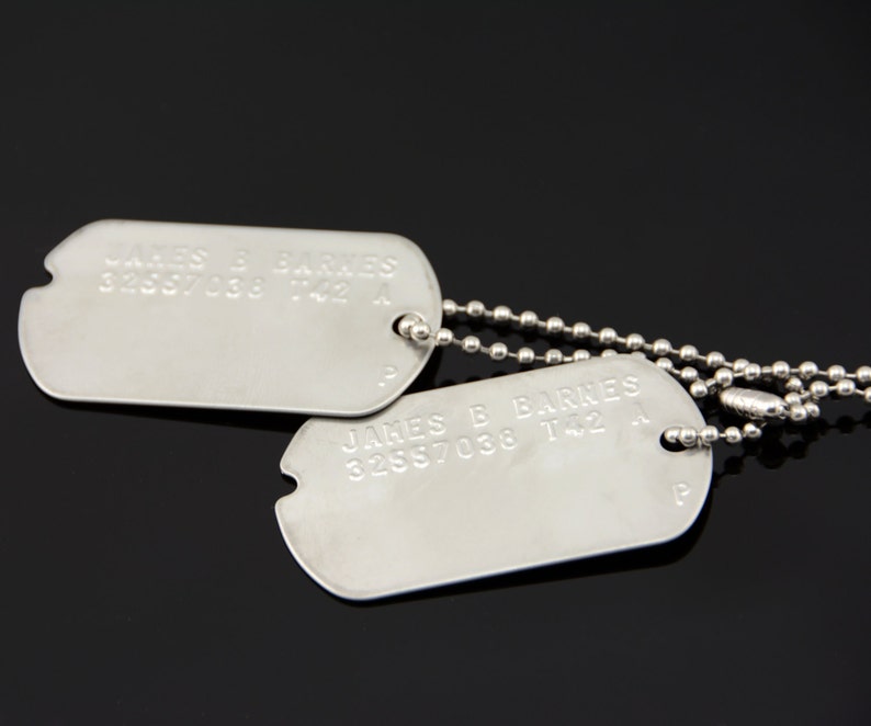 May include: Two silver dog tags on a silver chain. The top tag reads "JAMES B BARNES 32557038 T42 A". The bottom tag reads "JAMES B BARNES 32557038 T42 A".