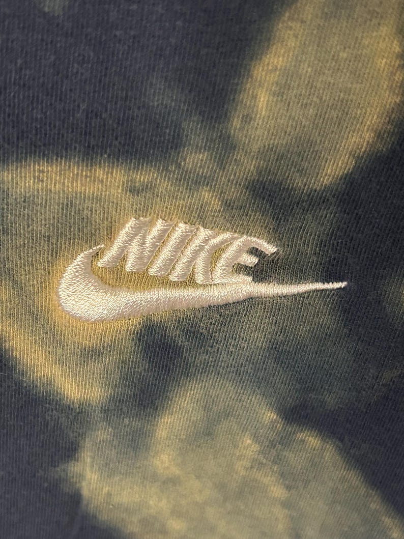 Puede incluir: Un logotipo Nike swoosh blanco bordado en una tela de tejido te&ntilde;ido anudado verde y amarillo.