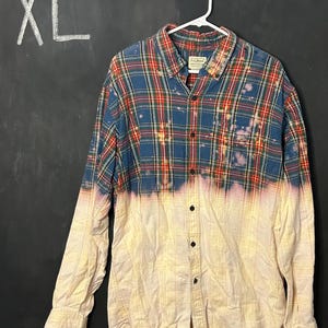 May include: A blue and red plaid flannel shirt with a white bleached ombre effect. The shirt is size XL and has a button-up front.