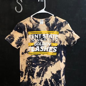Puede incluir: Una camiseta tie-dye en blanco y negro con el texto "Kent State University Golden Flashes" en amarillo.