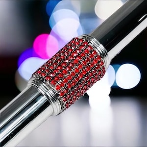 May include: A silver flute with a red rhinestone embellishment on the body. The flute is in focus, while the background is blurred and features out-of-focus lights.