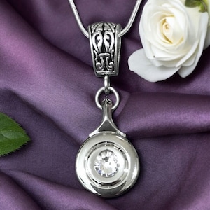 May include: A silver pendant necklace with a large, clear crystal set in a round, silver frame. The pendant is attached to a silver chain with an ornate, decorative bail.