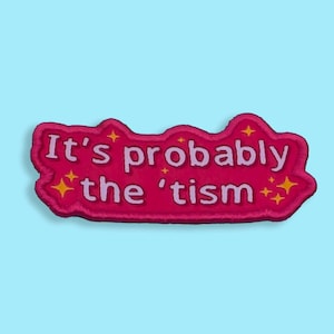 Può includere: Una toppa ricamata rosa con la frase "It's probably the 'tism" in lettere bianche. La toppa ha un contorno ondulato ed è decorata con stelle gialle. Lo sfondo è azzurro chiaro.