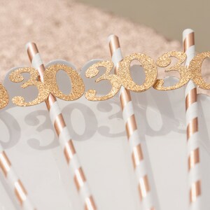 May include: Gold glitter number 30 cake toppers on white and gold striped paper straws.