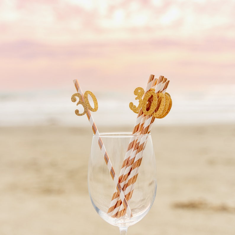 May include: Gold glitter number 30 straws in a clear glass. The straws are striped with brown and white.