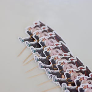 May include: A set of graduation cake toppers featuring cartoon images of people wearing graduation caps and gowns. Each topper is on a wooden stick.