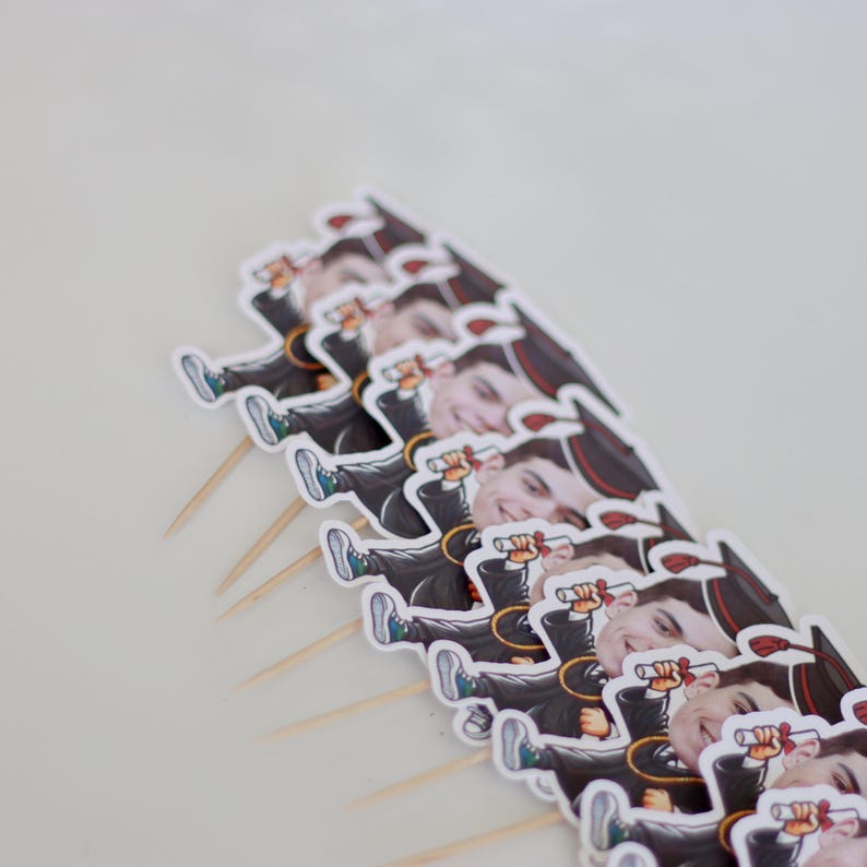 May include: A set of graduation cake toppers featuring cartoon images of people wearing graduation caps and gowns. Each topper is on a wooden stick.