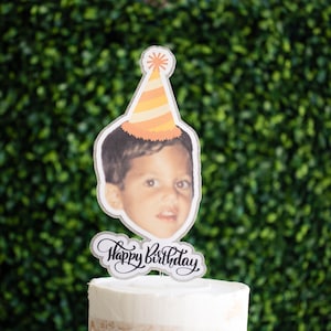 Może przedstawiać: Topper na ciasto ze zdjęciem młodej osoby w czapeczce urodzinowej w pomarańczowo-ż&oacute;łte paski. Napis "Happy Birthday" jest napisany kursywą pod zdjęciem, ze srebrną brokatową obw&oacute;dką.