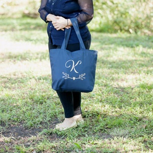 May include: A navy blue tote bag with a white embroidered letter "K" and a small heart with leafy branches on either side.