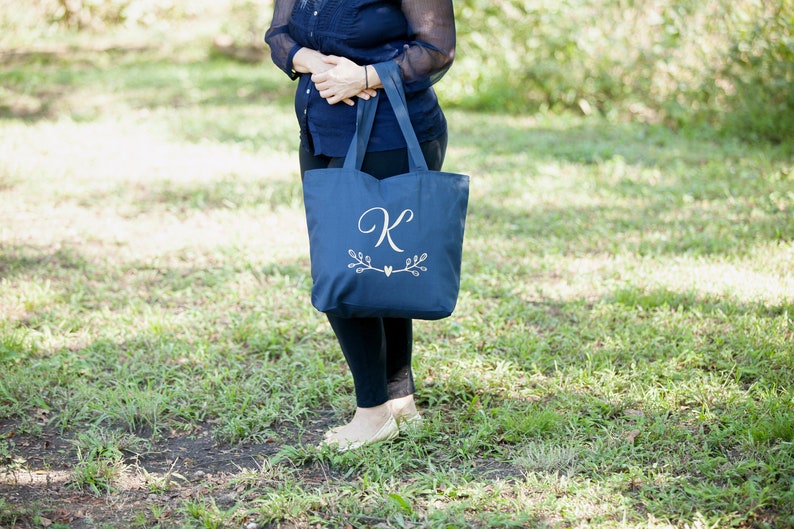May include: A navy blue tote bag with a white embroidered letter "K" and a small heart with leafy branches on either side.