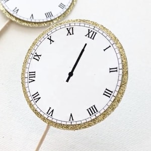 May include: Gold glitter clock face cupcake topper with Roman numerals and black hands pointing to midnight.