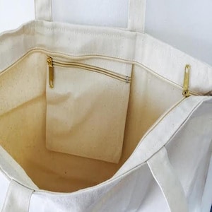 May include: A white canvas tote bag with a zippered pocket on the inside. The bag has two long handles.