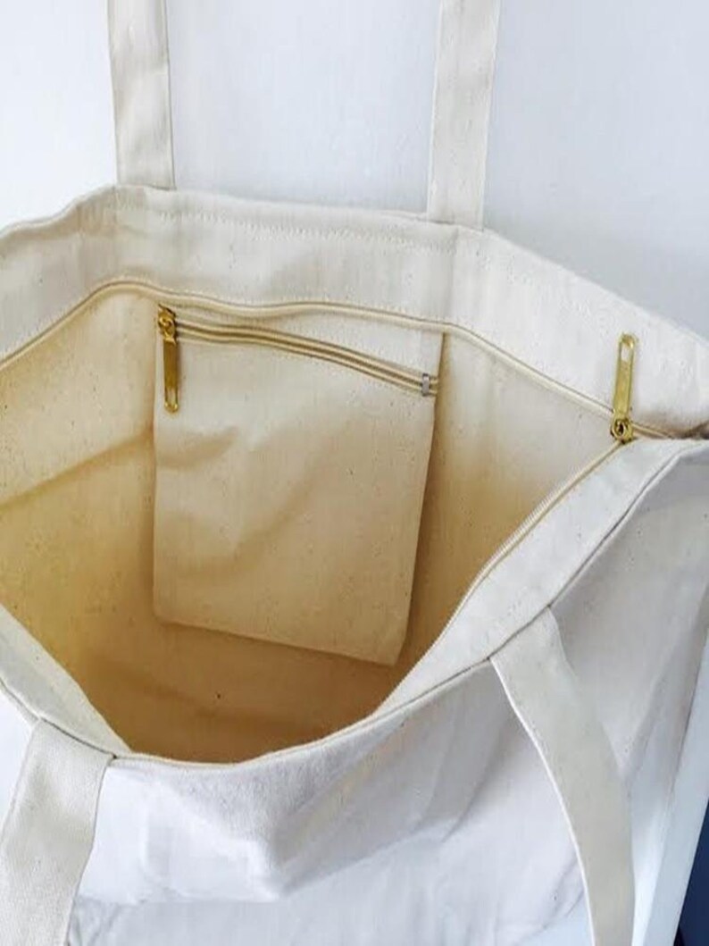 May include: A white canvas tote bag with a zippered pocket on the inside. The bag has two long handles.