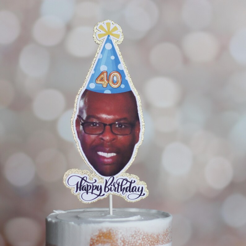 Może przedstawiać: Topper na ciasto z fotografią osoby w okularach i niebieskiej czapeczce urodzinowej z numerem 40. Słowa "Happy Birthday" są napisane kursywą pod zdjęciem. Topper jest ozdobiony złotym brokatem.