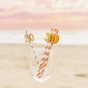 May include: A clear glass with gold glitter straws decorated with the numbers "30" for a birthday celebration.