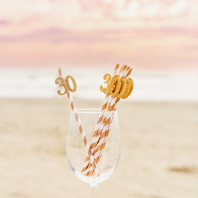 May include: A clear glass with gold glitter straws decorated with the numbers "30" for a birthday celebration.