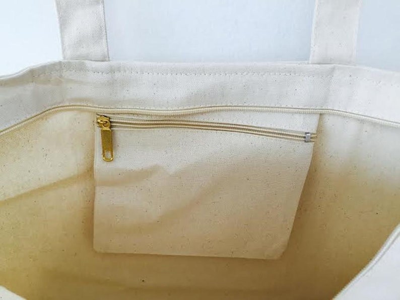 May include: A white canvas tote bag with a zippered pocket on the inside. The zipper is gold metal.