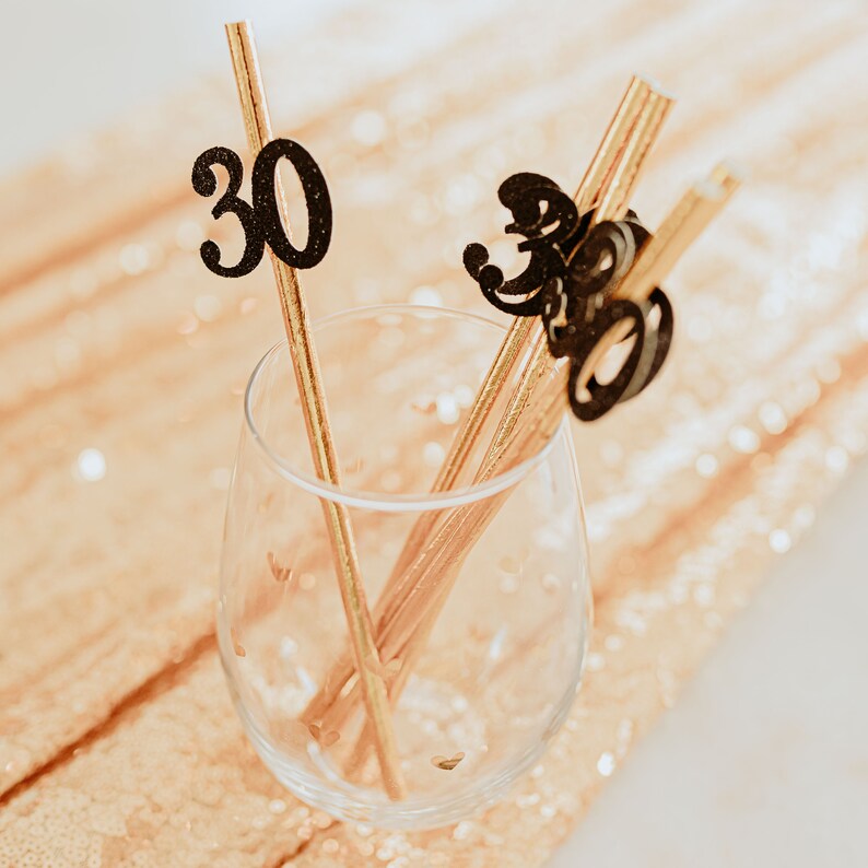 May include: A glass with gold straws and black glitter paper decorations that say "30" in a glass.