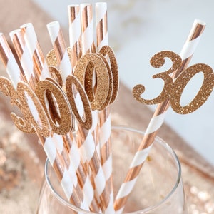 May include: A set of gold glitter straws with the number "30" on them. The straws are in a clear glass. The straws are perfect for a 30th birthday party.