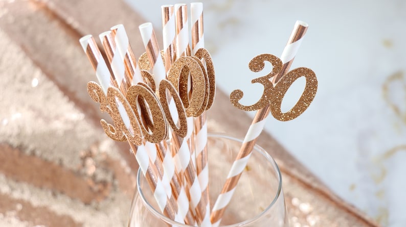 May include: A set of gold glitter straws with the number "30" on them. The straws are in a clear glass. The straws are perfect for a 30th birthday party.