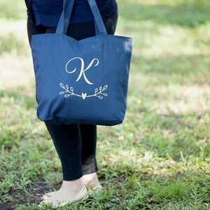 May include: A navy blue tote bag with a white monogram of the letter "K" and a small heart with branches on either side.