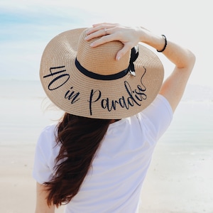 May include: A straw sun hat with a black ribbon and the text "40 in Paradise" written in black script.