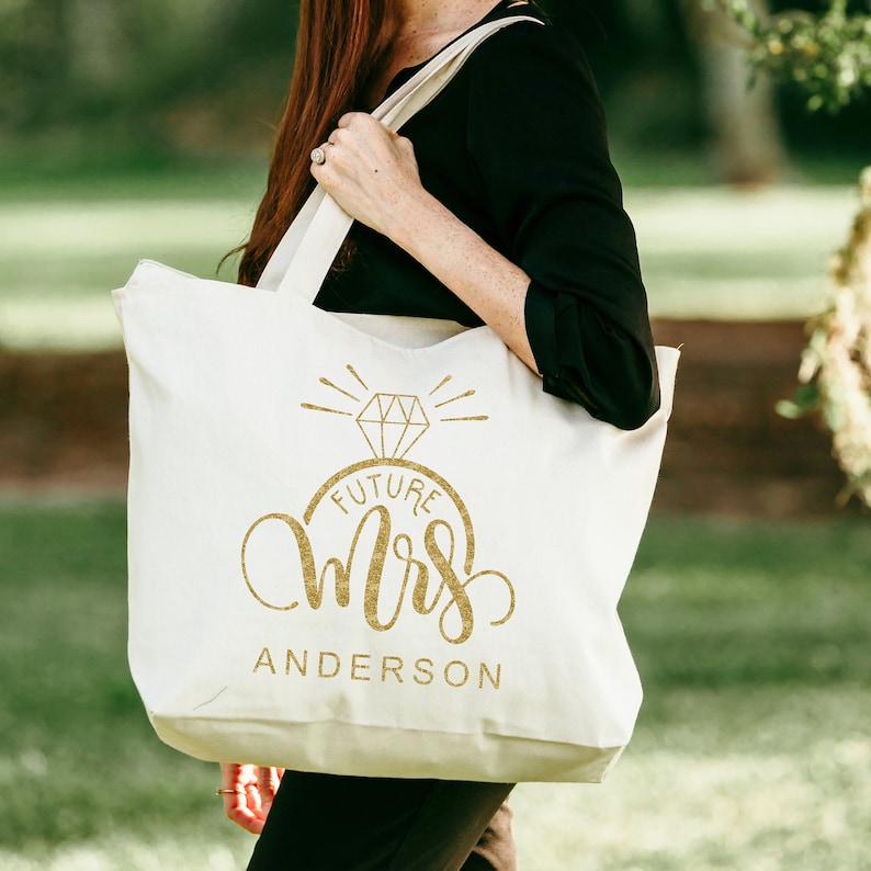 May include: White canvas tote bag with gold lettering that says "Future Mrs. Anderson" with a diamond ring graphic.