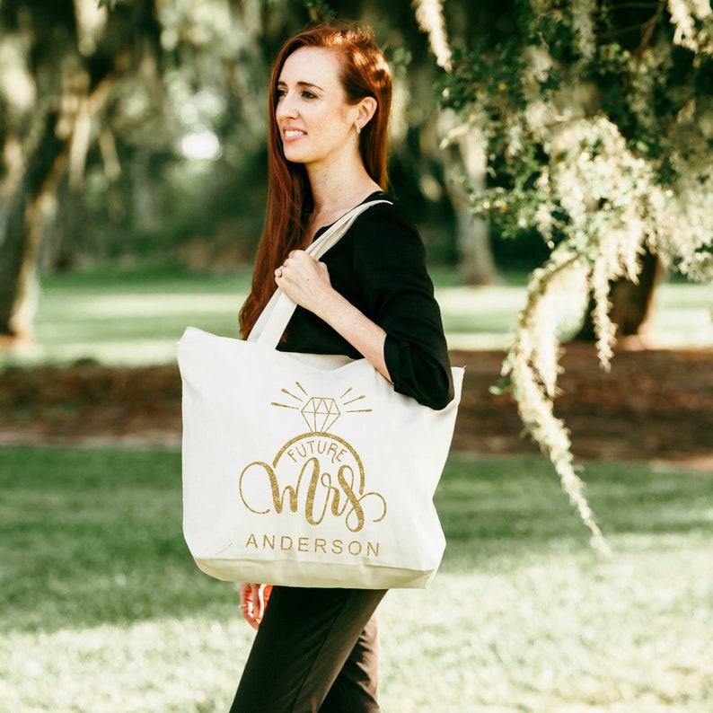May include: A white canvas tote bag with a gold glitter design that says "Future Mrs. Anderson" with a diamond ring graphic above the text.