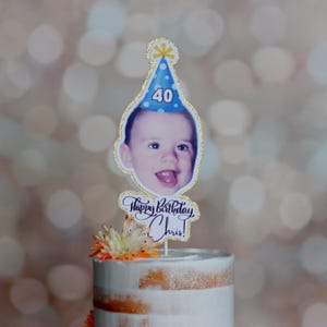 Może przedstawiać: Topper na tort urodzinowy ze zdjęciem osoby w niebieskiej czapeczce urodzinowej z numerem 40. Topper ma złoty brokatowy kontur, a pod zdjęciem widnieje napis "Happy Birthday Chris!".