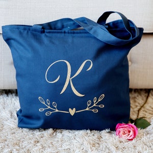 May include: A navy blue tote bag with a gold glitter letter "K" and a heart design. The bag has two handles and is made of canvas.
