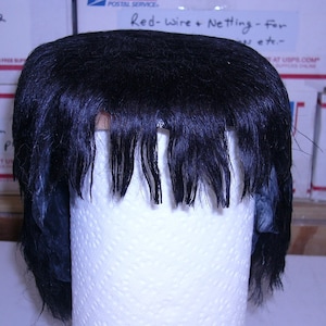 May include: Black wig with a straight fringe on a white styrofoam head.