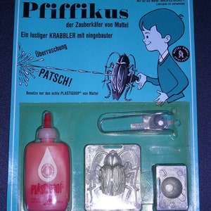 May include: A blue and white cardboard box with the text "Pfiffikus" in black. The box contains a toy beetle kit with a mold, a small bottle of red liquid, and a pair of tweezers. The text "Ein Mattel MACH-ES-SELBST Zubehör-Satz" is printed on the box.